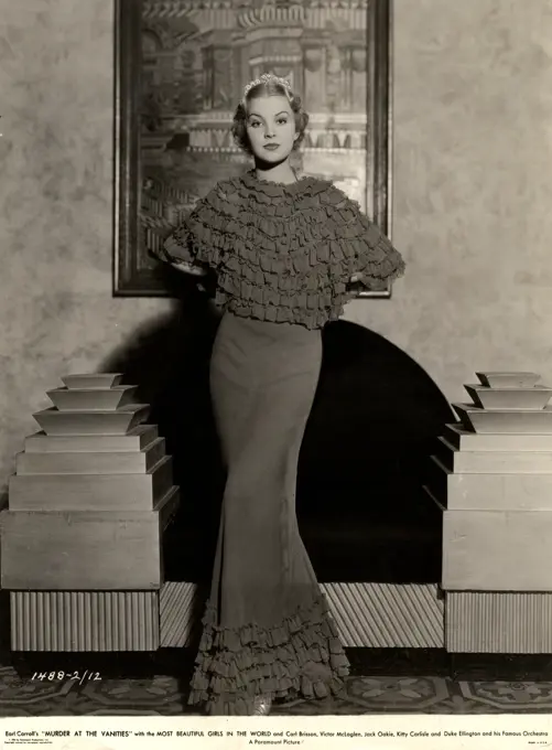 Portrait of young woman posing in long, frilly dress by armchair, 1931