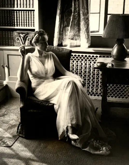 Young woman in white dress smoking cigarette while sitting in armchair