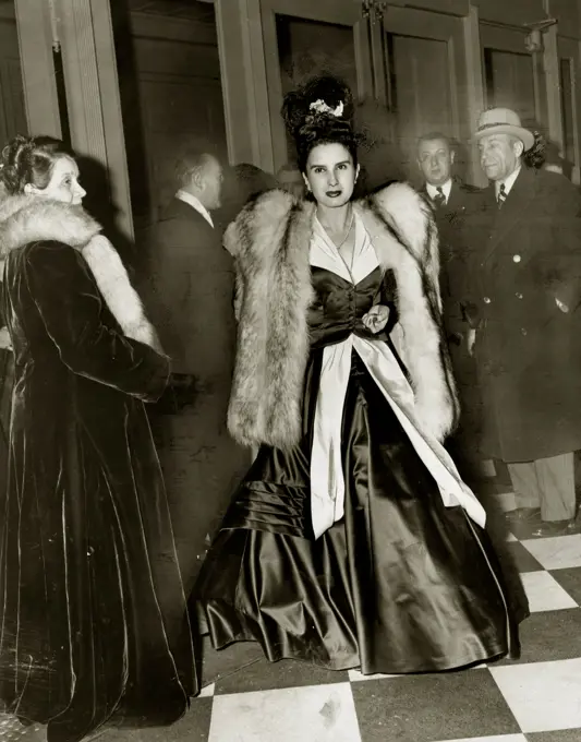 Young woman wearing ball gown and fur coat, people in background