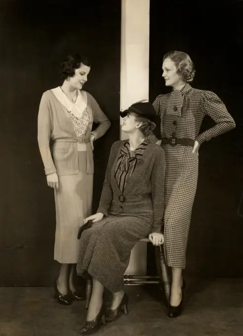 Three women posing in studio, one sitting