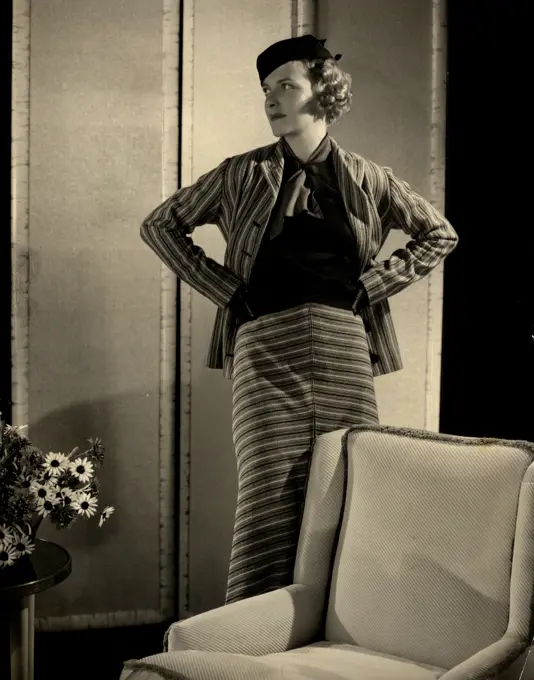 Young woman in striped outfit posing by armchair