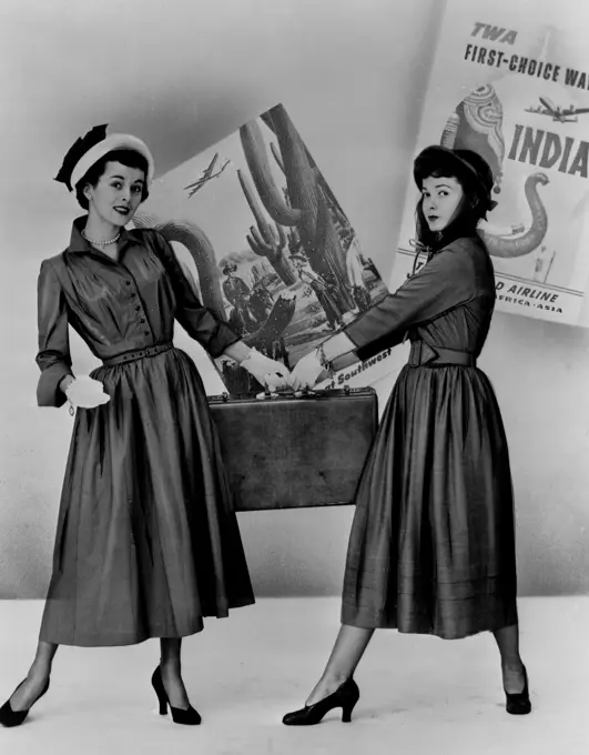 Two fashion models posing with suitcase, posters in background