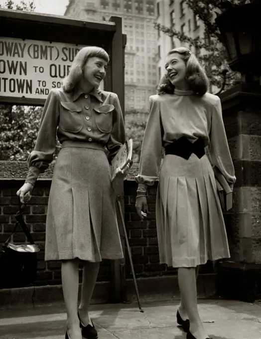 Two young women walking on street in elegant clothing, smiling face to face