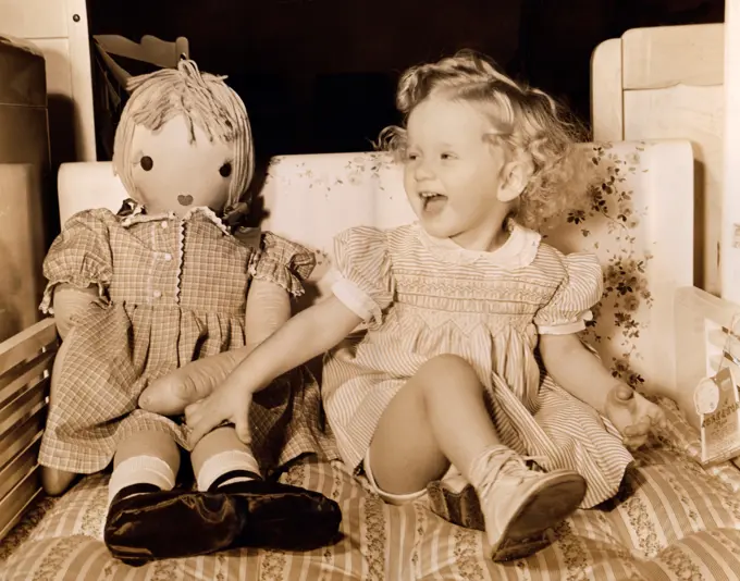 Girl sitting with her doll and laughing