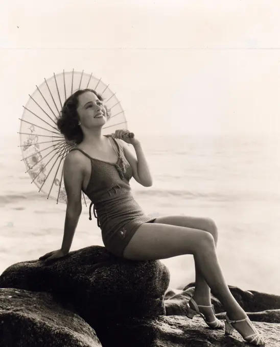 Attractive woman wearing swimming suit sitting on boulder on beach