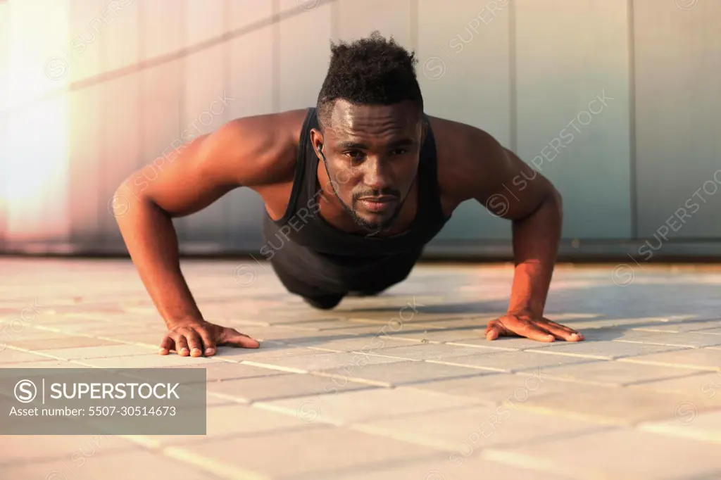 African man in sports clothing keeping plank position in beach while exercising outdoors, at sunset or sunrise.