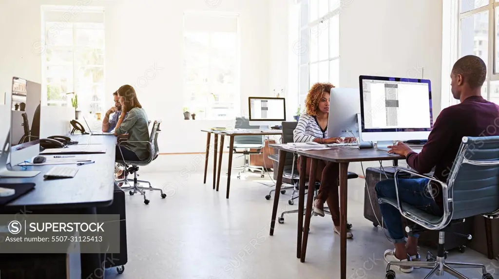 Working in an open plan office. Shot of colleagues working on their computers in an open plan office.