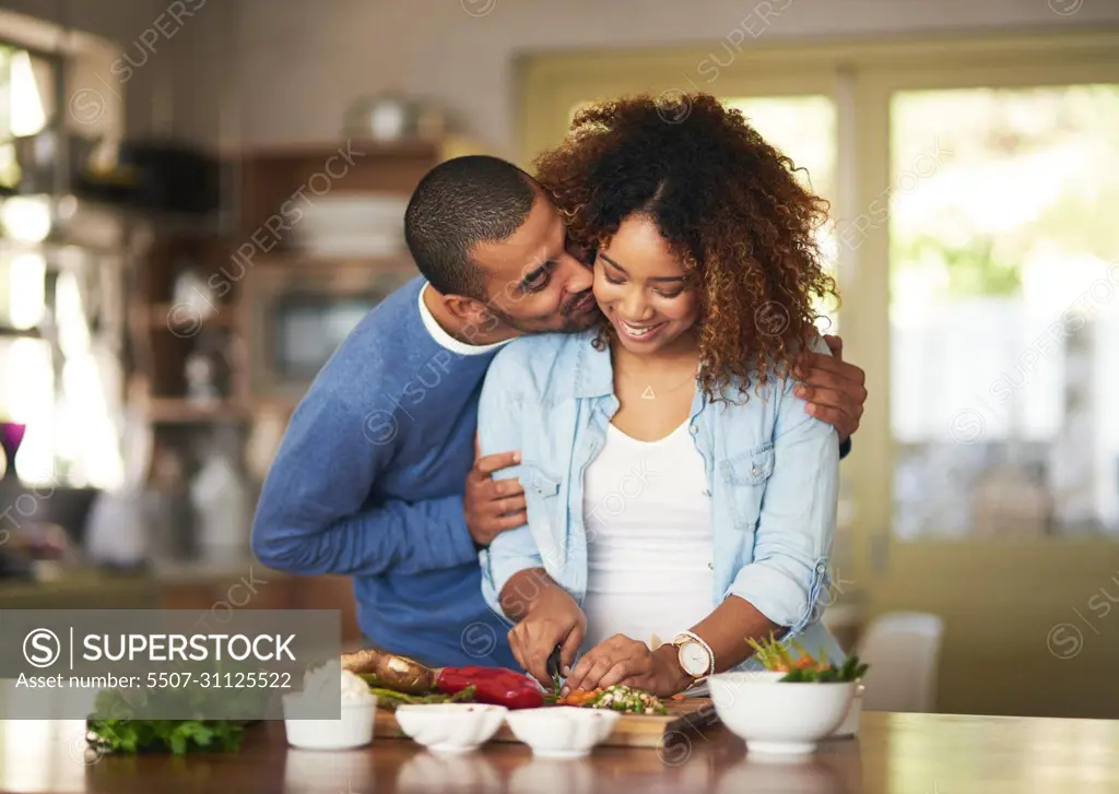 The healthy marriage is a happy marriage. Shot of a young man kissing his wife while she prepares a healthy meal at home.