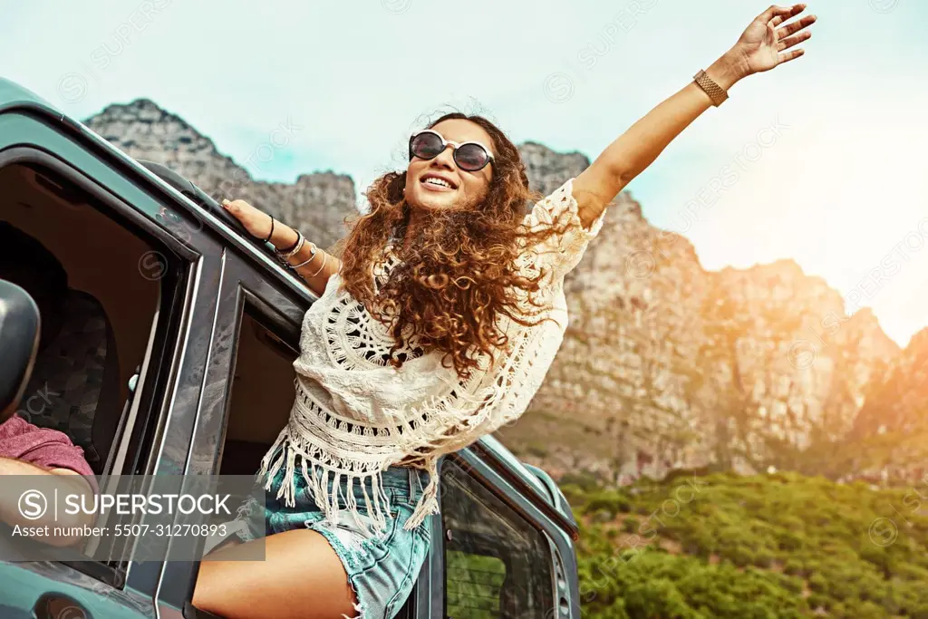 Bring on the good times. Cropped shot of a young woman leaning out a car with her arms outstretched while on a roadtrip.