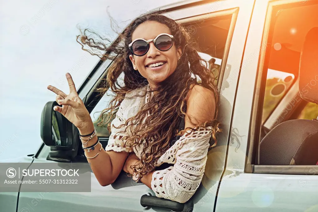 Peaceful times on the go. Portrait of a young woman leaning out the window of a car while on a roadtrip.