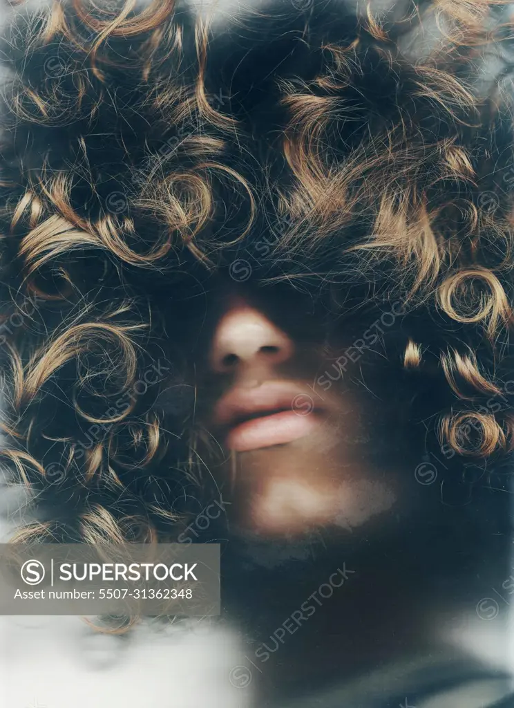 Hiding within himself. Young man with his face obscured by his long, curly hair.