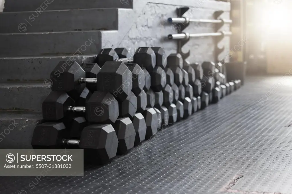 Closeup of a group of gym weights on the floor in an empty health and sports club. Macro view of dumbbells barbell weights in a dark exercise room. Get to the gym to increase your health and fitness