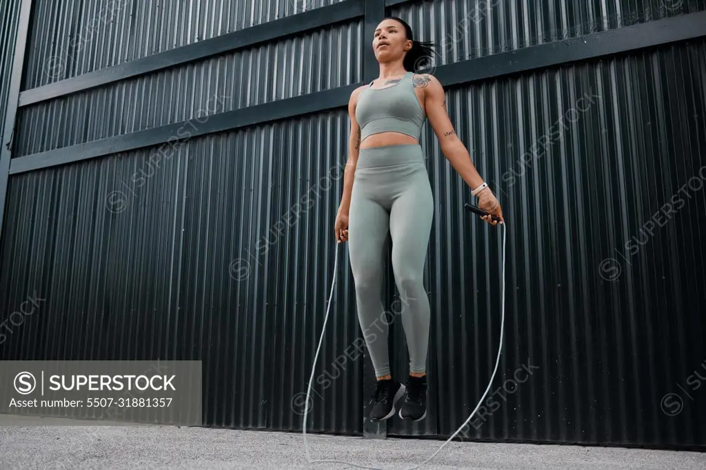 One young african american female athlete skipping using jump rope while exercising outside in the city. Beautiful and dedicated mixed race sportswoman working out alone against an urban background