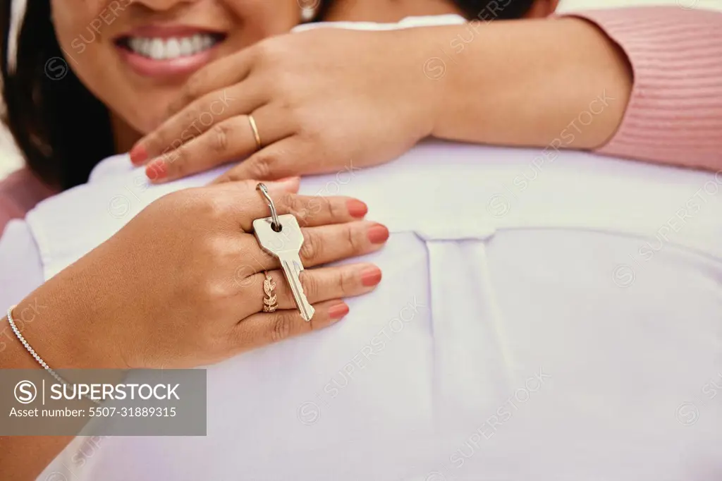 Closeup woman hugging husband while holding house keys. Loving mixed race couple celebrating after buying new of first home together. Woman receiving key to apartment. Couple moving in together