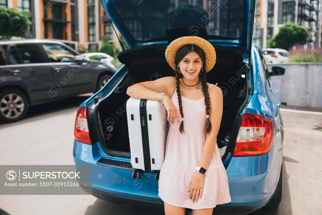 Woman packing her suitcase into luggage boot of the car.