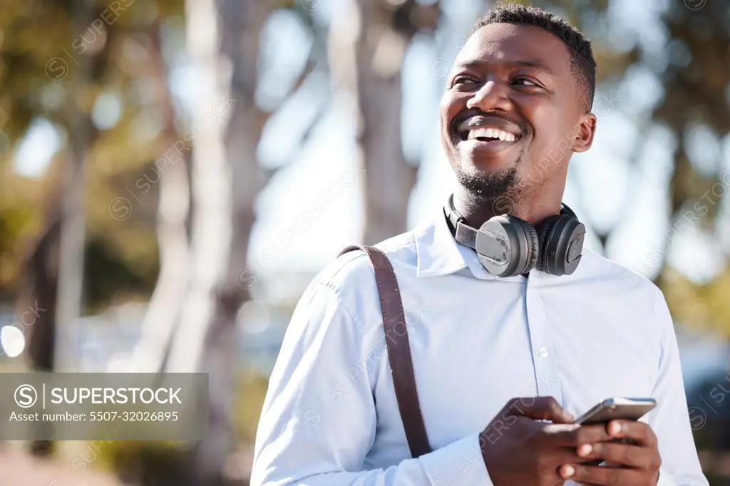 Happy african american businessman wearing headphones and texting on a cellphone while commuting in the city. One young black guy looking thoughtful while using apps and browsing social media online