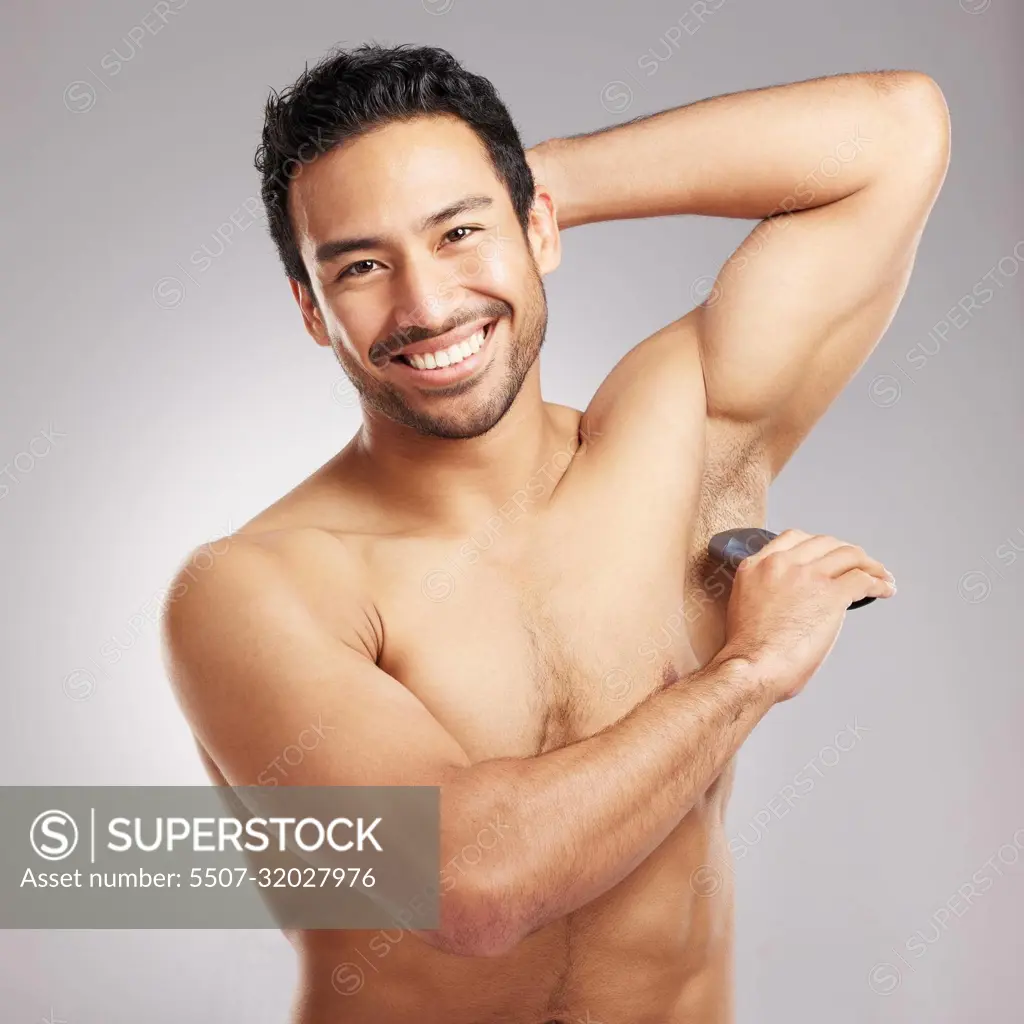 Handsome young mixed race man shirtless in studio isolated against a grey  background. Hispanic male using an electric razor to shave his underarms.  Healthy and fresh, shaving is part of his grooming -