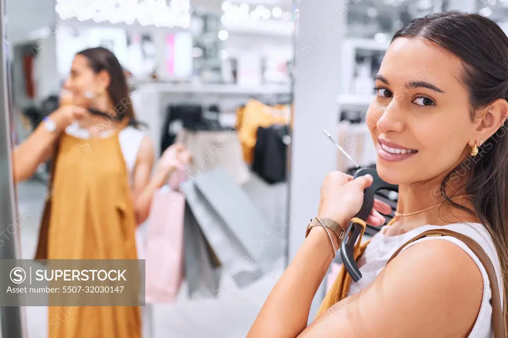 Portrait of a trendy young woman holding a dress against her deciding whether to buy it. Smiling female fitting on clothes in a store. Mixed race shopper happy about finding a sale and discount