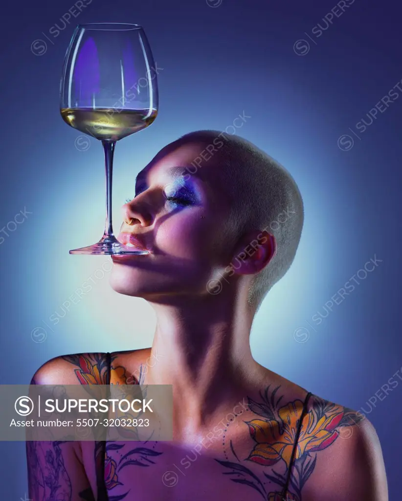 Im a goddess thats as fine as wine. Studio shot of an attractive young woman wearing edgy makeup and holding a glass of wine in her mouth against a blue background.