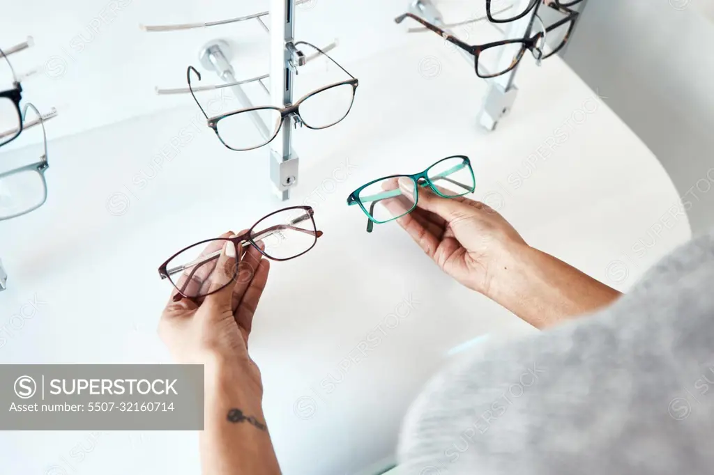 Buying, looking and shopping for glasses at a retail eyewear store and optometrist inside. Customer holding shop stock trying to decide on a new modern style, trendy and stylish frames to buy on sale