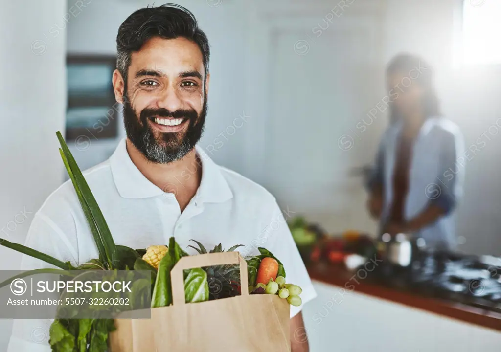 Buy healthy, eat healthy. Portrait of a happy man holding a bag of fresh vegetables while standing in his kitchen.