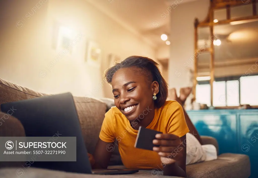 Online shopping young, happy and smiling African lady with bank, credit or gift card. Excited, comfortable and cheerful ethnic female typing on laptop searching, browsing and buying present from home