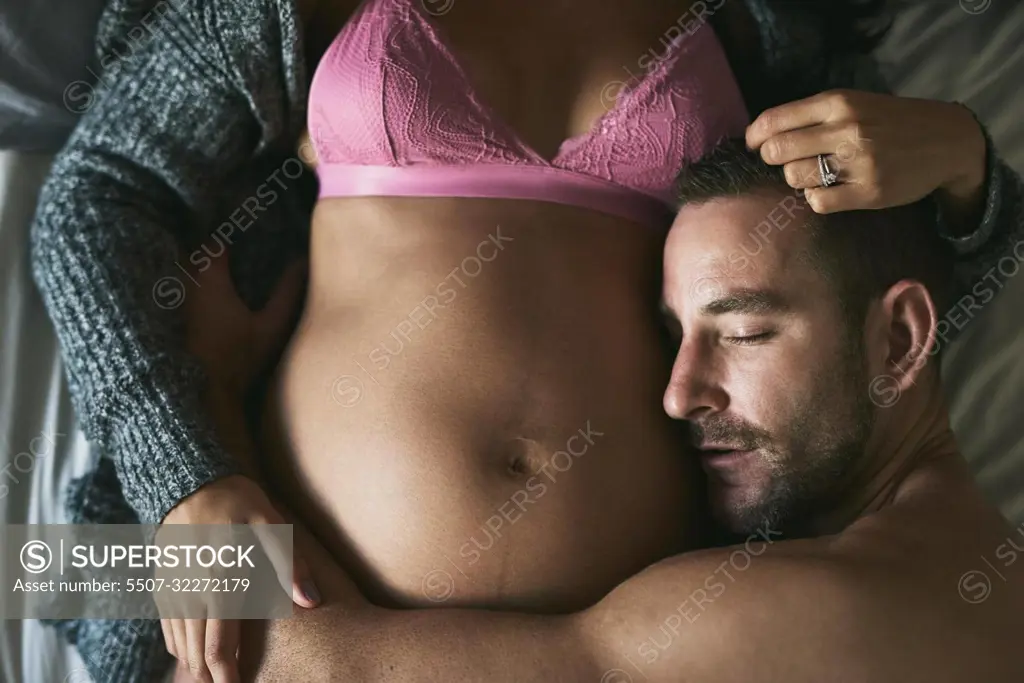 In love with his unborn child. High angle shot of a handsome young man loving his pregnant wife in their bedroom.