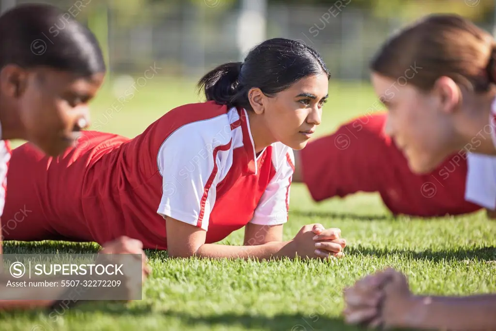 Women soccer players in a team doing the plank fitness exercise in training together on a practice sports field. Healthy female group of young athletes doing a core strength workout using teamwork