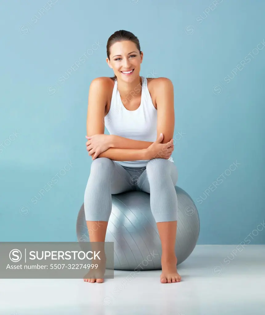 This ball is my health secret. Studio portrait of a healthy young woman sitting on an exercise ball against a blue background.