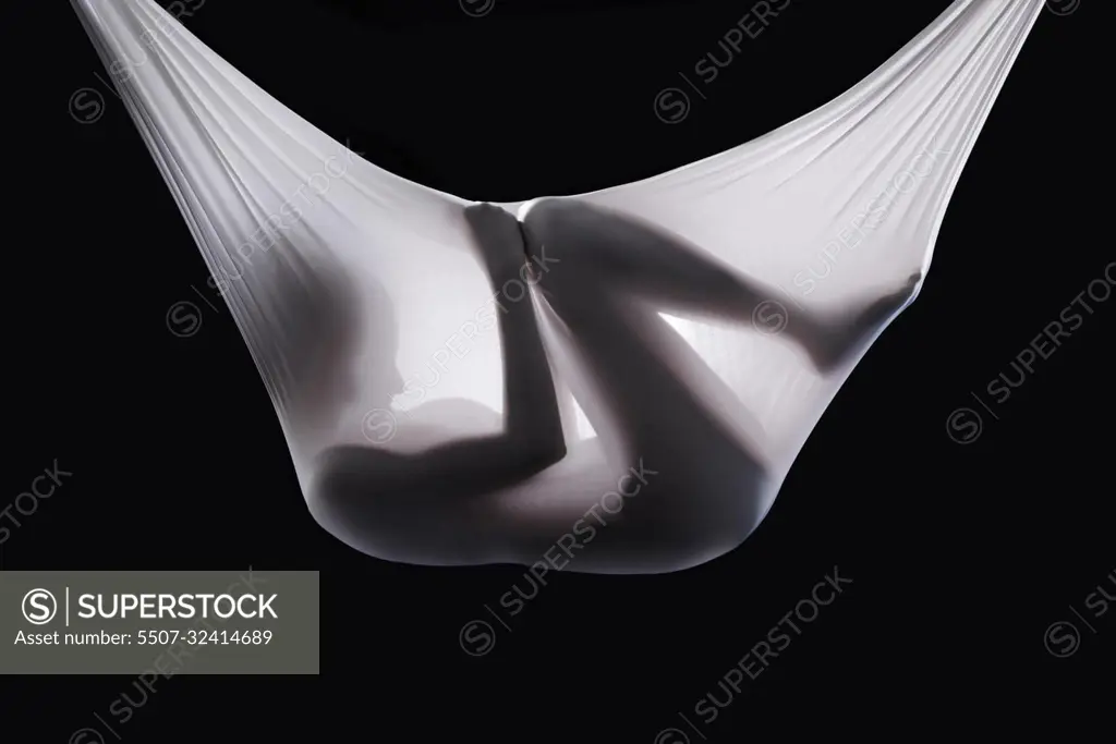 You can fly but that cocoon has to go. Studio shot of a woman wrapped in fabric in a fetal-like position.