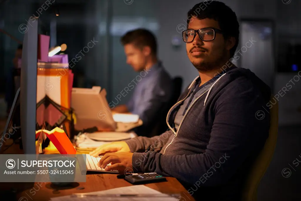 Getting the job done. a group of young coworkers working in a dimly-lit office.