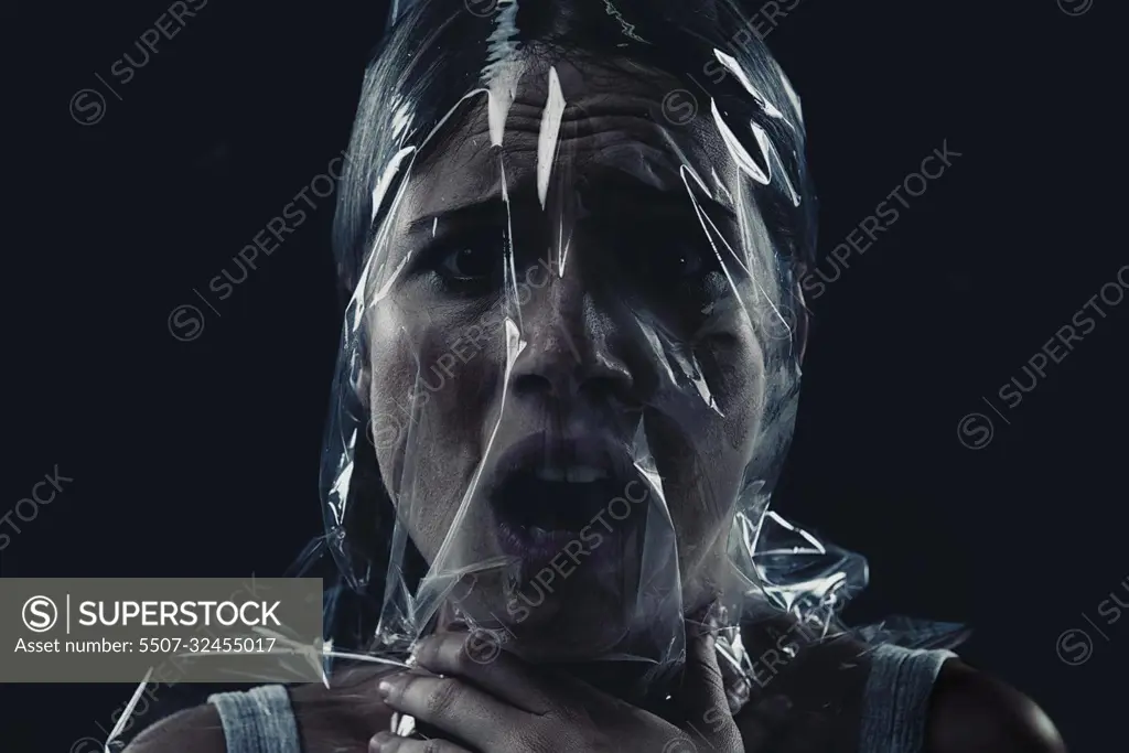 Fighting for oxygen, fighting for her life. A young woman suffocating with her head wrapped in plastic while isolated on a black background.