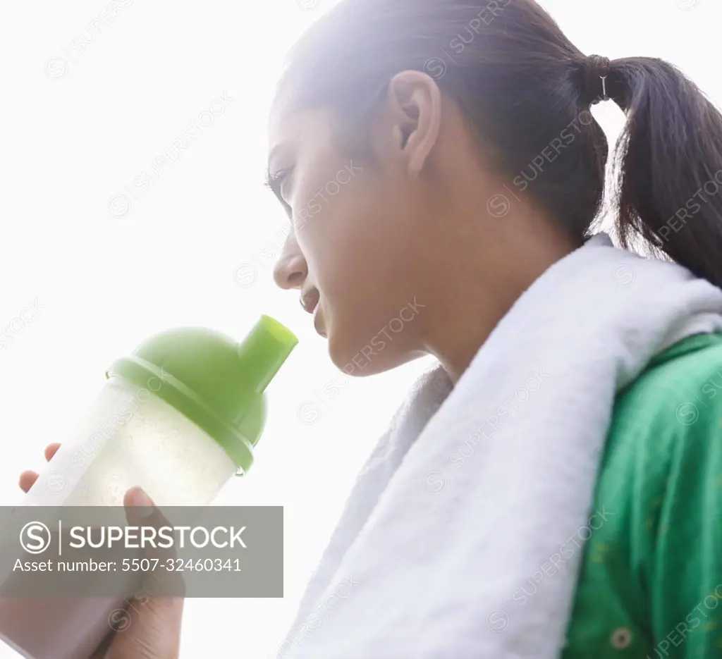 Staying healthy. A young ethnic woman drinking a sports drink outdoors.