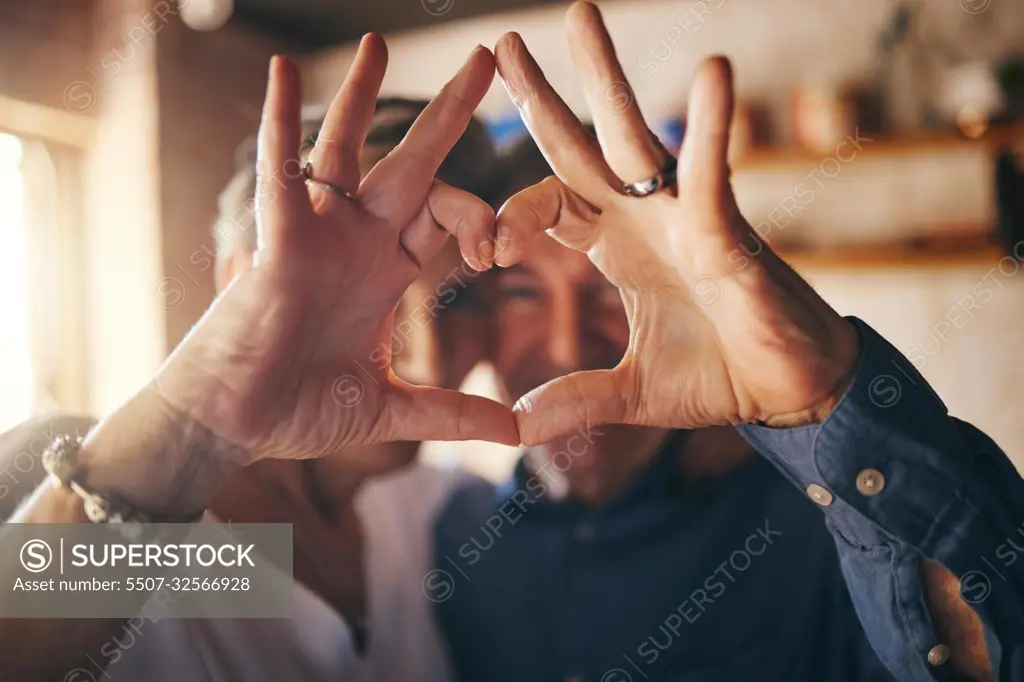 Love, hands and heart sign with senior couple relax and bonding in their home together, cheerful and in love. Support, soulmate and loving man and woman sharing romantic moment and enjoy relationship