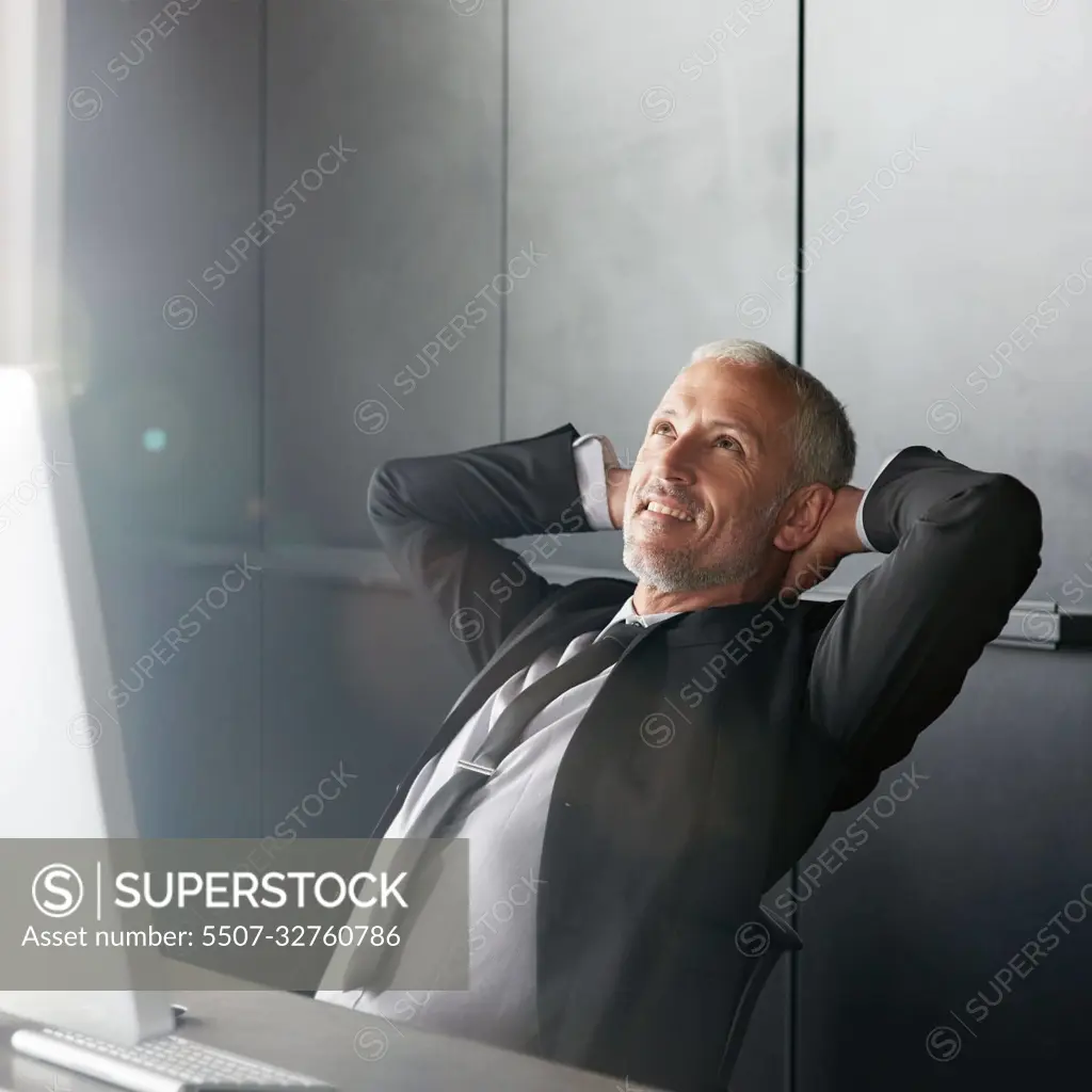 Taking a short break. a handsome mature businessman sitting in the office  with his arms behind his neck. - SuperStock