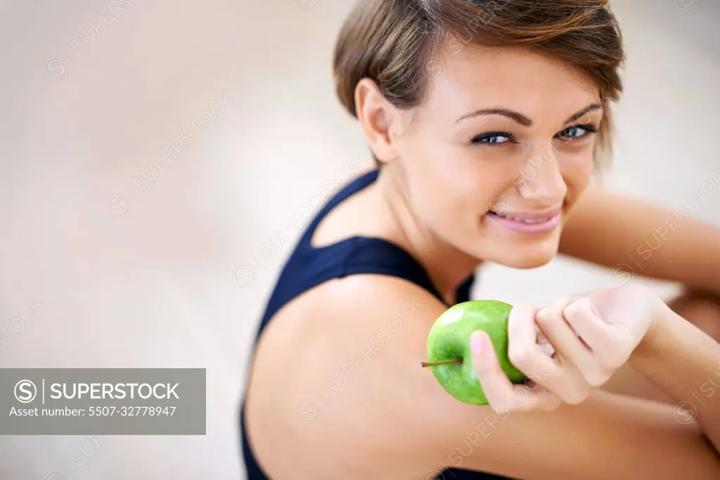 Building blocks for a happy healthy life. a sporty young woman sitting on a gym floor eating an apple.