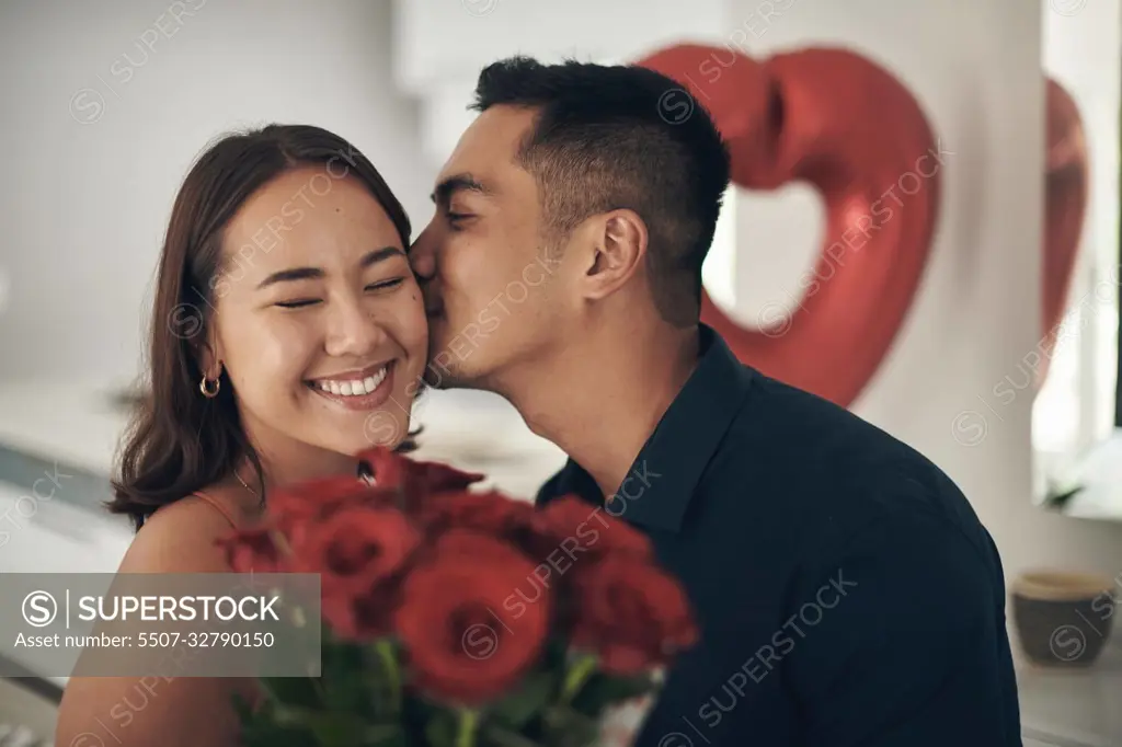 Love, rose and valentines day with a couple kissing in their home, in celebration of romance. Dating, flower boquet or surprise with a man and woman in a house to kiss while bonding in intimacy