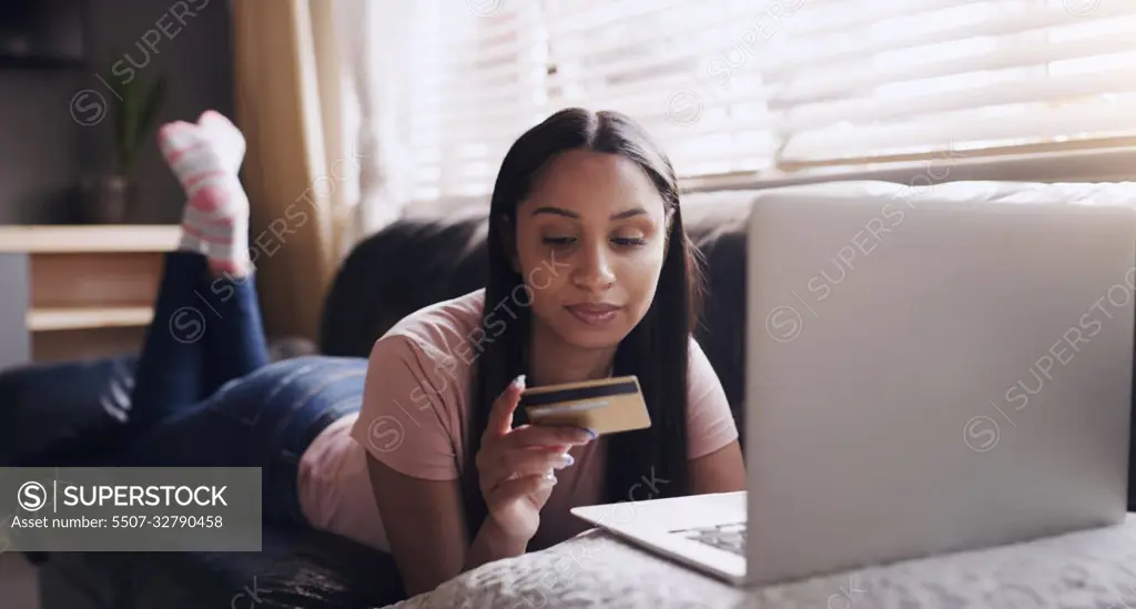 To buy or not to buy. a young woman relaxing while doing some online shopping at home.