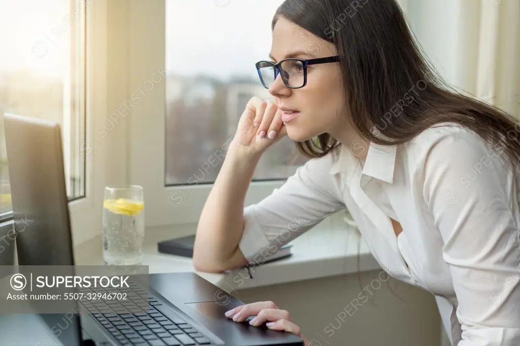 Young business woman with glasses working on laptop computer at home