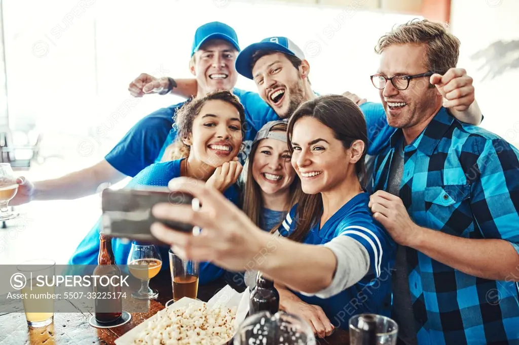 Kicking off the game with a selfie. a group of friends taking a selfie while watching a sports game at a bar.