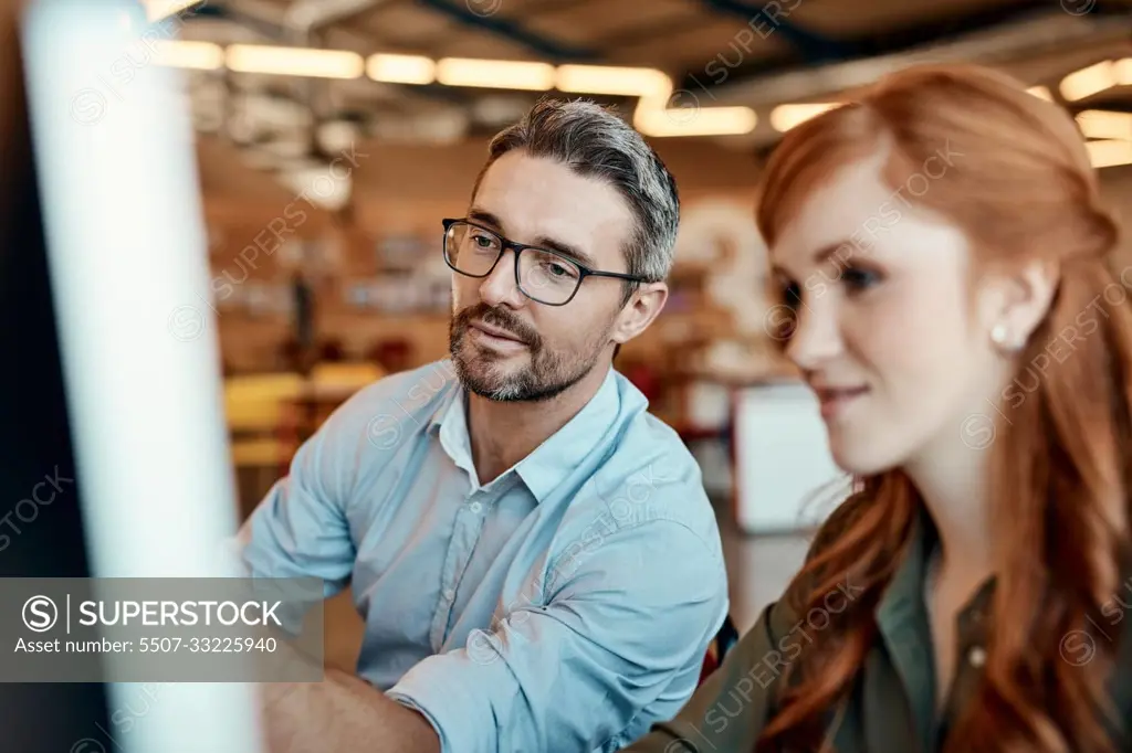 Working together, its just better. a young businesswoman and mature businessman using a computer together in a modern office.