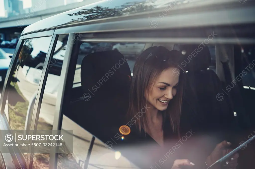 Work begins before she gets to the office. a young businesswoman using a digital tablet while traveling in a car.