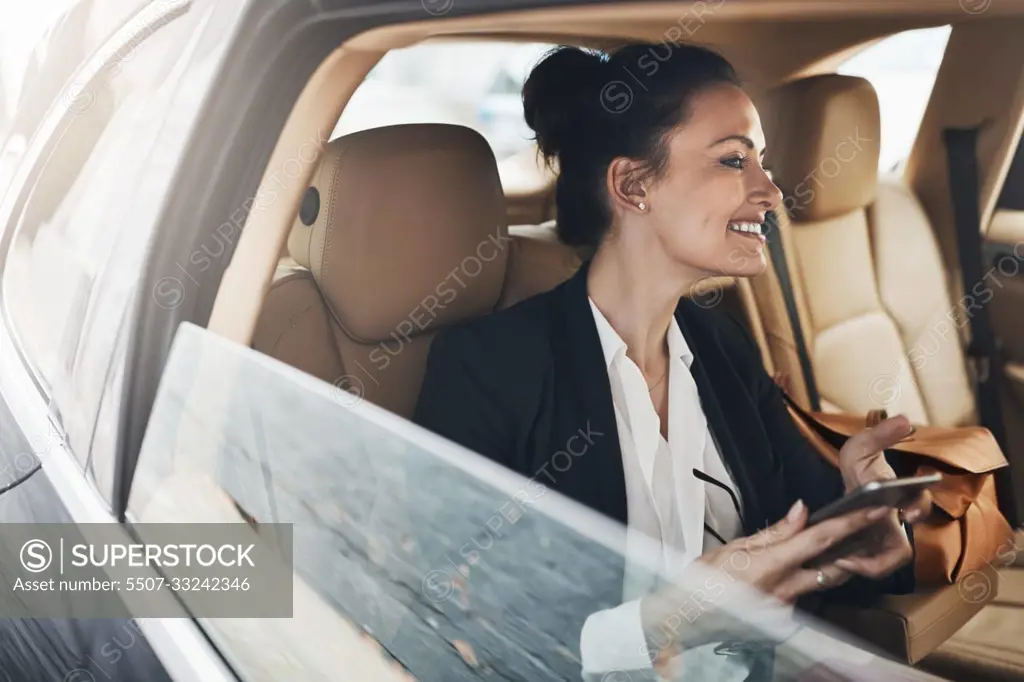 I am excited to get working. a cheerful young businesswoman seated in a car as a passenger while texting on her phone on her way to work.