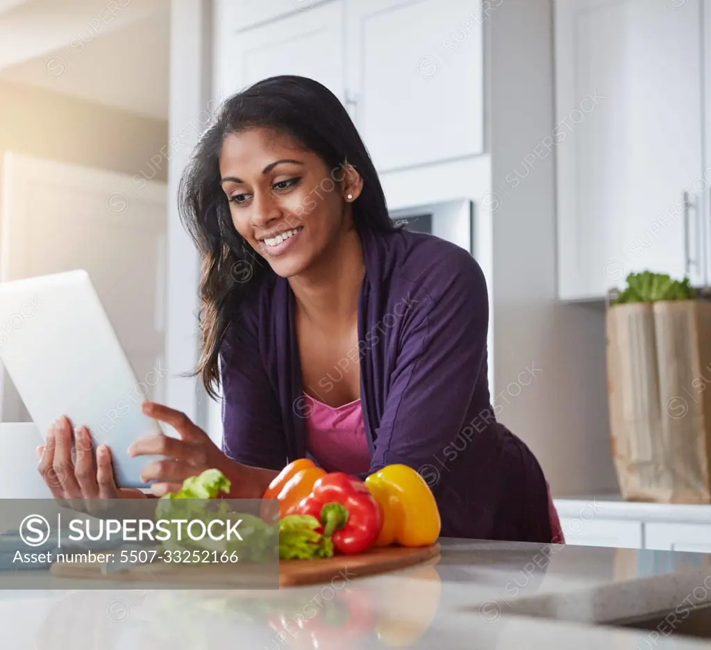 Loaded with recipes for a healthy lunch. a young woman using a digital tablet while preparing a healthy meal at home.