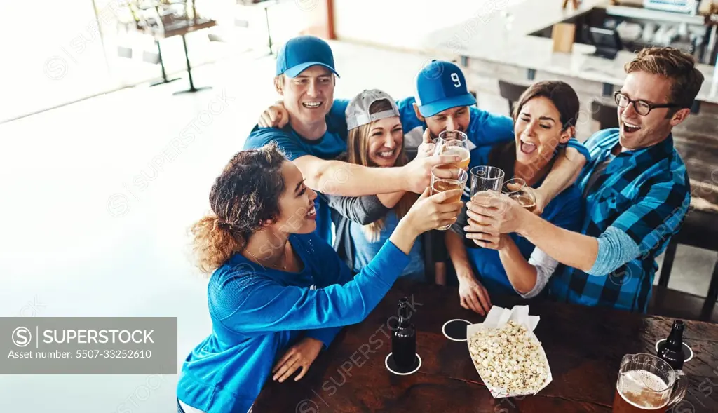 Sports fans make up a sports family. a group of friends toasting with beers while watching a sports game at a bar.