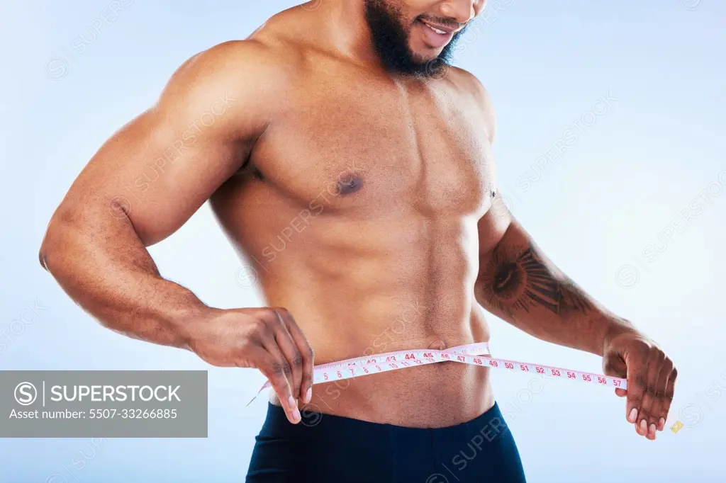 Black man, exercise and body, weightloss and measuring tape with health and active lifestyle on blue background. Shirtless male bodybuilder, abs and fitness with diet, healthy and strong in studio