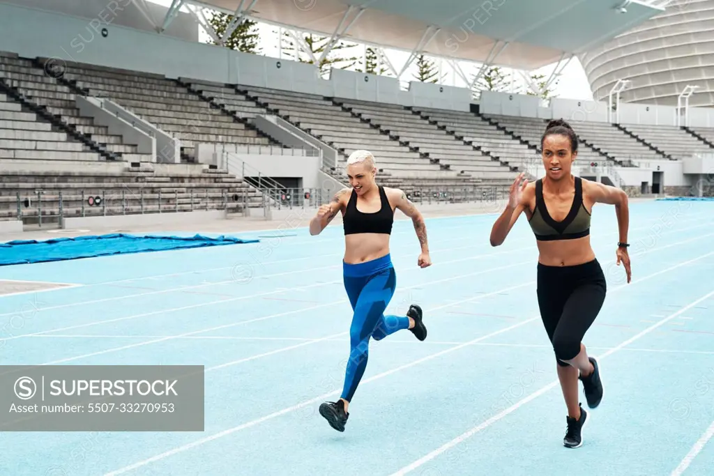 There is no finish line too far away. Full length shot of two attractive young athletes running a track field together during an outdoor workout session.