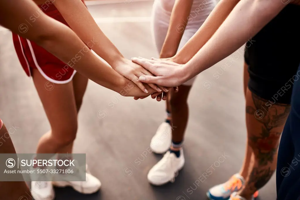 On three. an unrecognizable group of sportswomen piling their hands together before a basketball game.