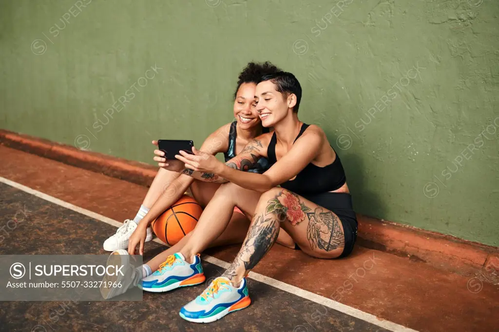 Lets get another selfie. two attractive sportswomen sitting together for a selfie after a basketball game during the day.