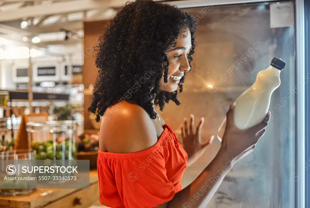 Woman, grocery shopping or reading milk label for sales date, vitamin information or calcium data in Brazilian store retail. Happy smile, supermarket customer or nutritionist and dairy fridge product